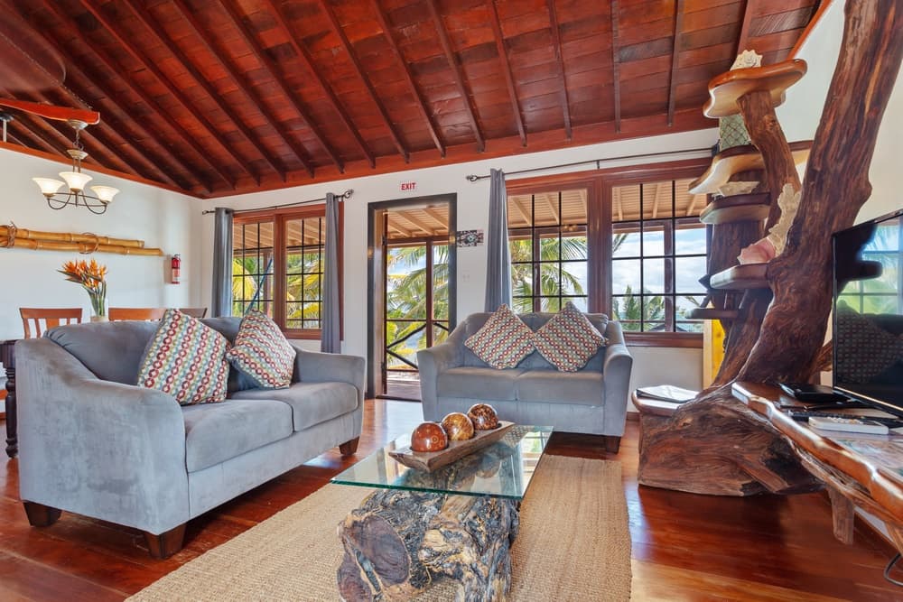 A cozy living room with two gray sofas, a unique coffee table made from a tree trunk, and large windows leading to an outdoor view.