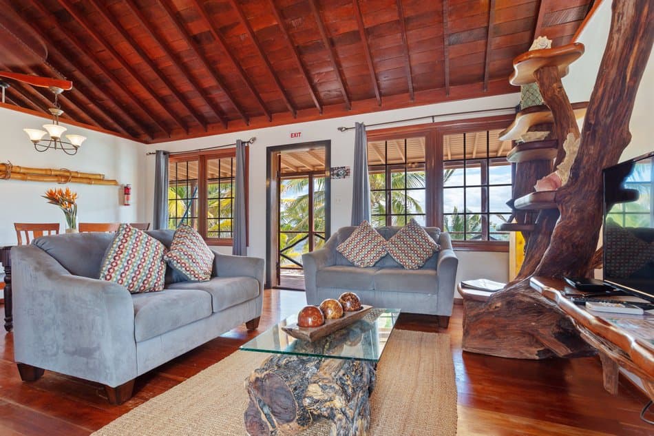 A cozy living room featuring gray sofas with patterned cushions, a glass coffee table, and large windows that invite natural light.