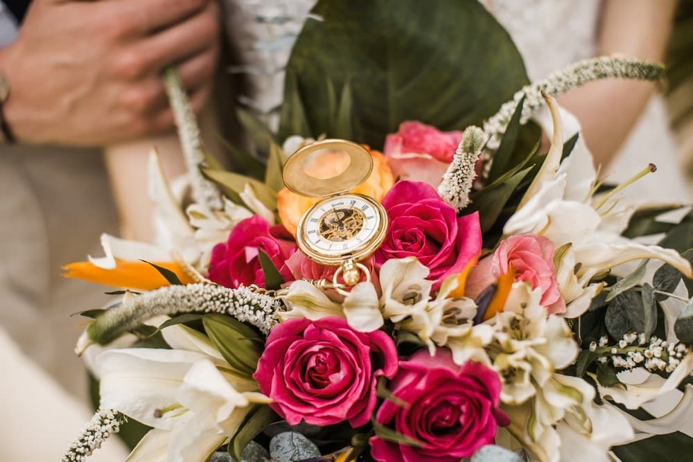 A close-up of a bouquet featuring vibrant roses and lilies, with an antique pocket watch nestled among the flowers.