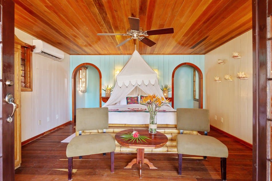 A cozy bedroom featuring a canopied bed, wooden ceiling, and tropical decor.