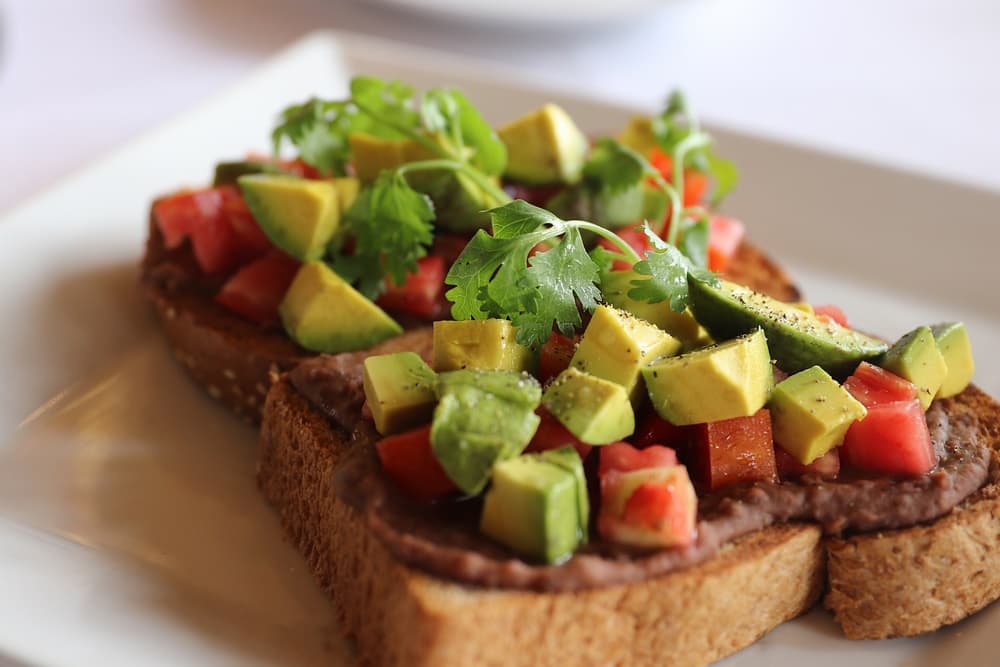 Toasted bread topped with refried beans, diced tomatoes, avocado, and cilantro.