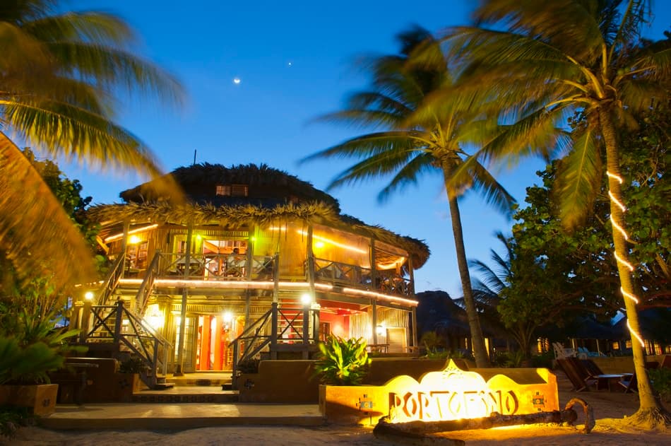 A tropical beachfront restaurant with palm trees, illuminated at dusk.