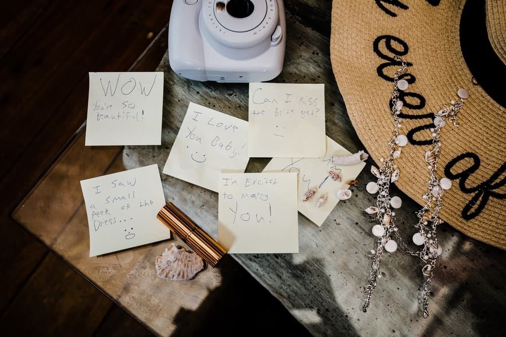 A flat lay of handwritten love notes, a camera, a hat, and jewelry arranged on a wooden table.