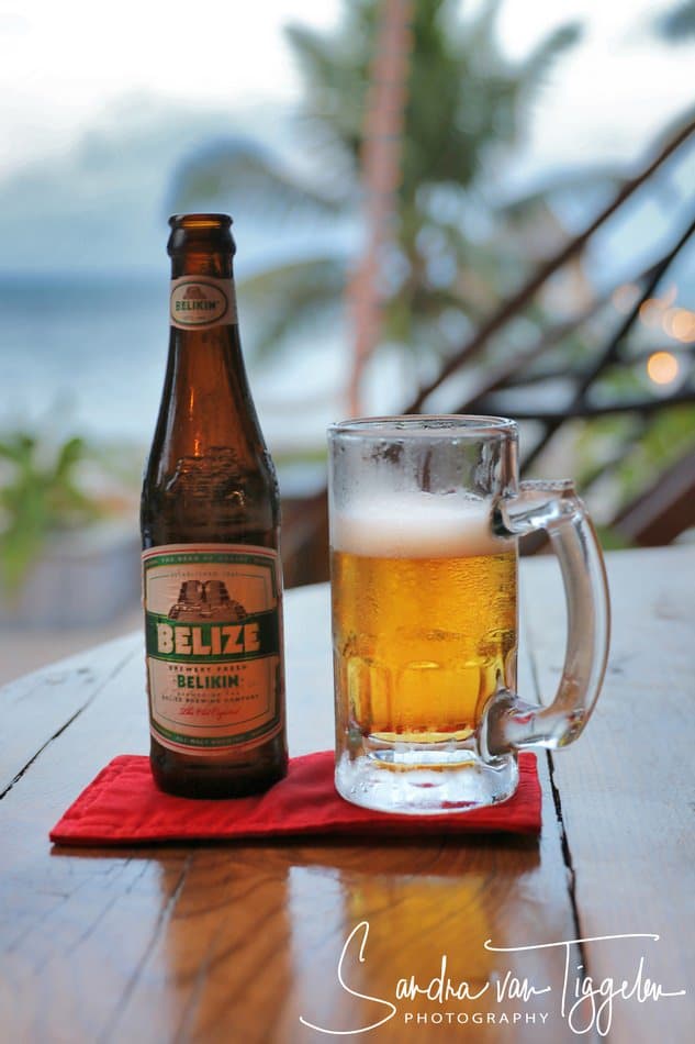 A bottle of Belikin beer next to a frosty glass of beer on a wooden table.