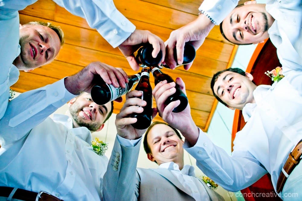 Five men in white shirts cheer with beer bottles, seen from below.