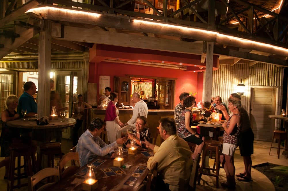 A lively bar scene with patrons socializing, dining, and enjoying drinks in a warmly lit environment.