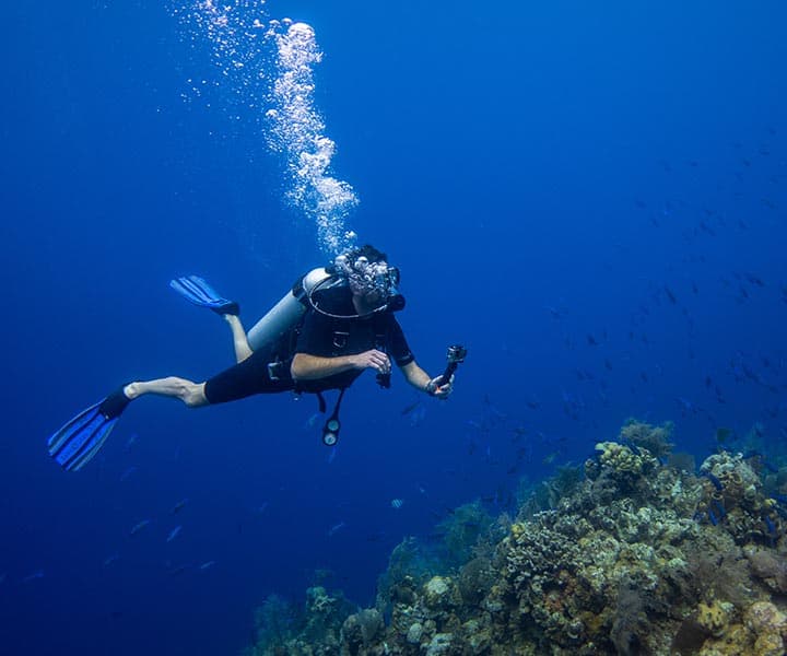 A diver underwater wearing a scuba tank and scuba mask with bubbles floating to the surface.