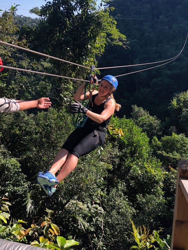A woman zip-lining through a lush green forest.