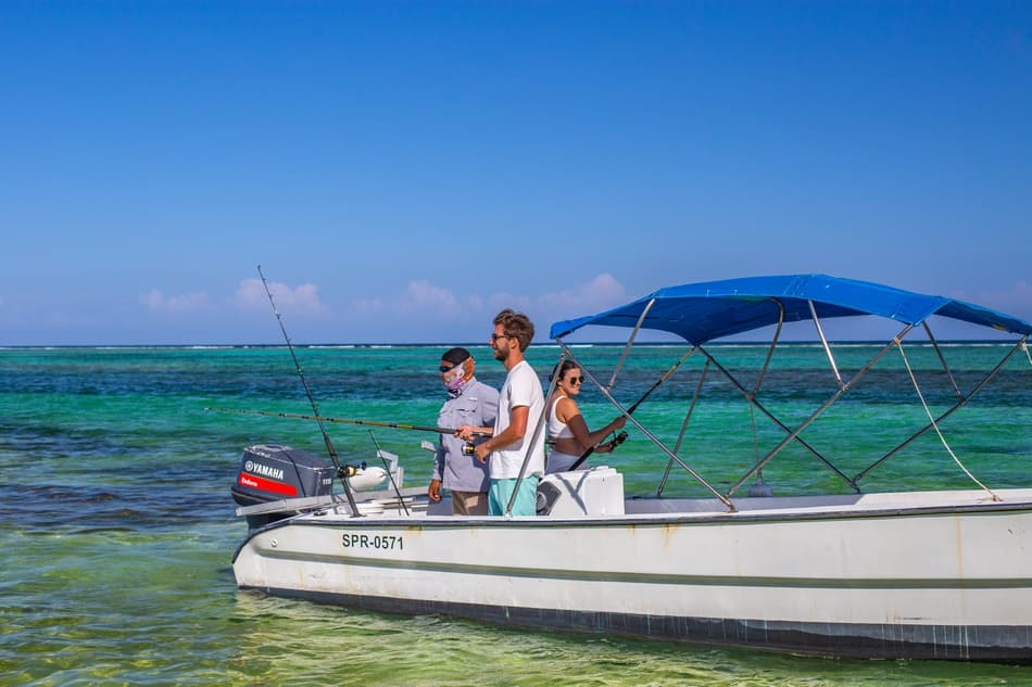 Four people fishing on a small boat in clear turquoise waters under a blue sky.