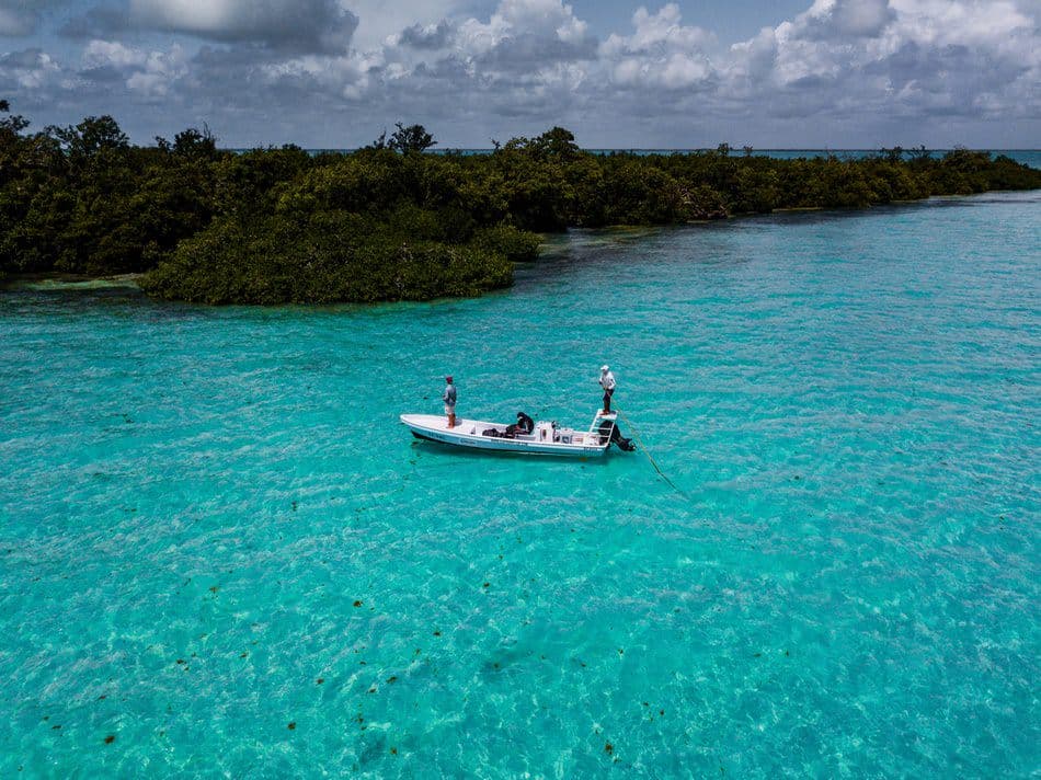 A small boat floats on clear turquoise waters near a lush green coastline.