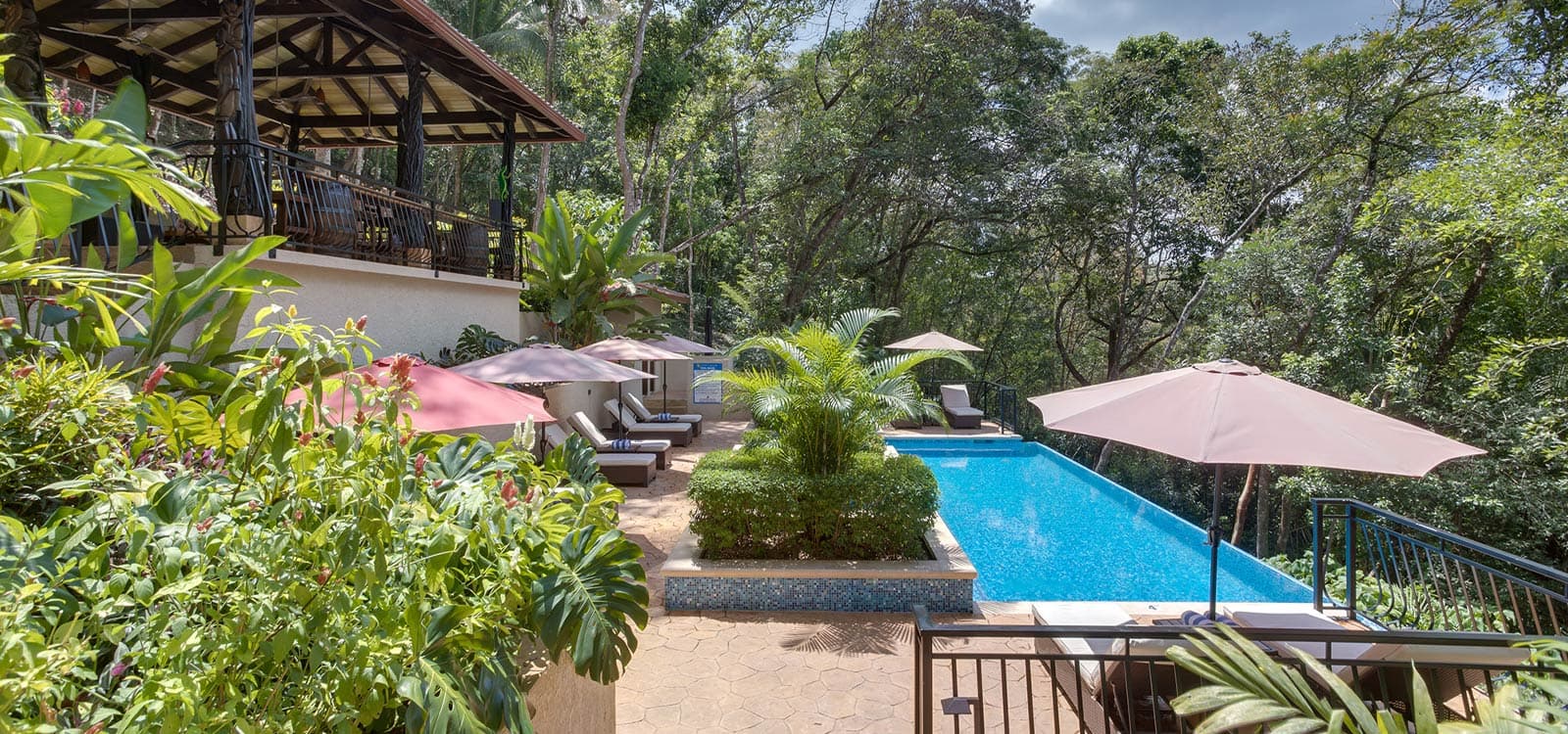 A serene tropical poolside with lush greenery, lounge chairs, and umbrellas. The setting is tranquil and luxurious, surrounded by dense forest.